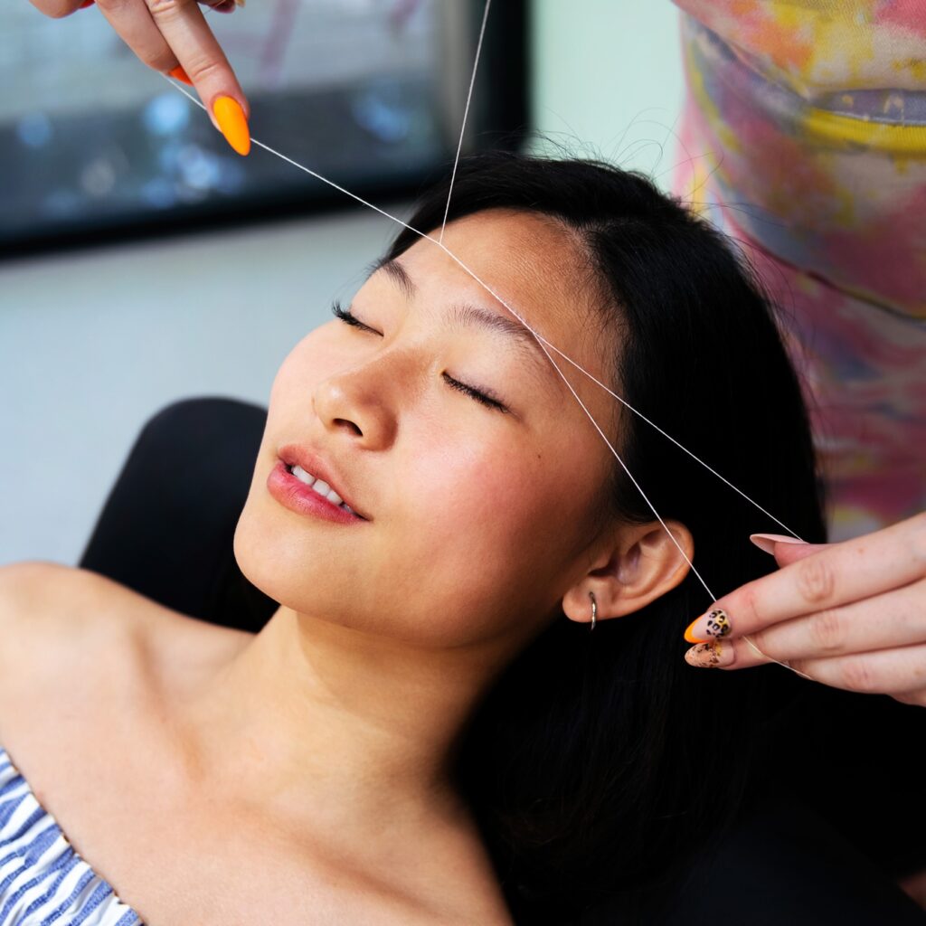 beautician performs eyebrow threading on a woman