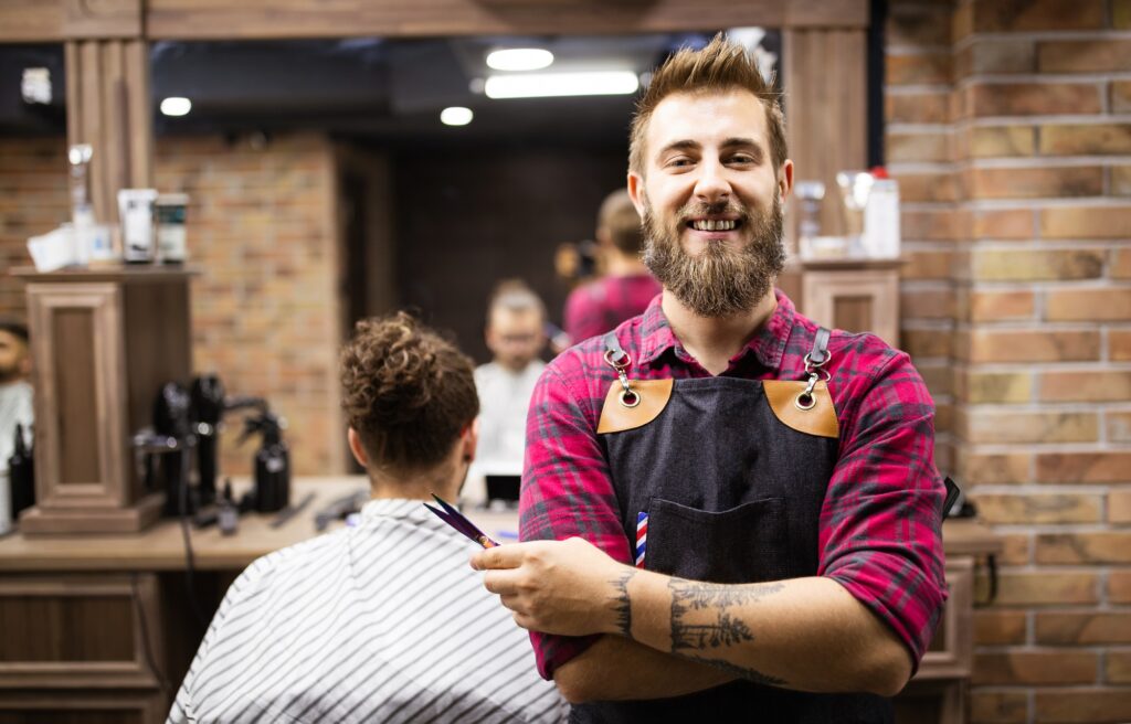 Portrait of happy young barber with client at barbershop and smiling