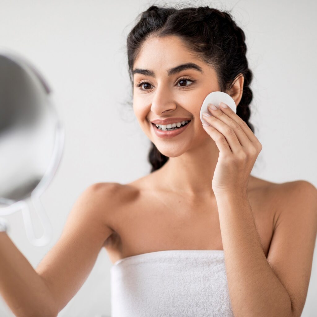 Skincare Routine. Smiling Young Indian Woman Cleansing Skin With Cotton Pad